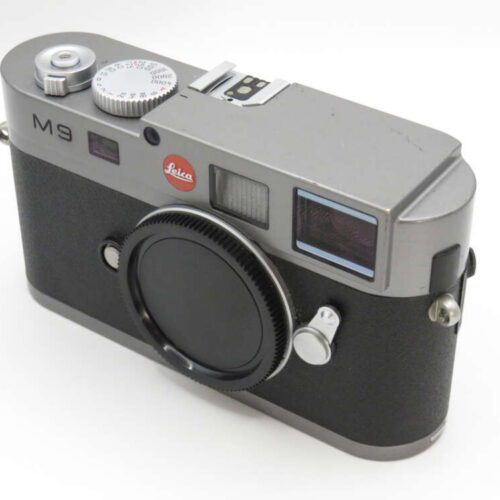 A silver and black Leica M9 camera featuring a prominent lens mount cap and various control dials on top.