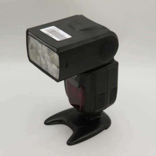 A black external camera flash with a rectangular head sits on a stand, against a plain background.