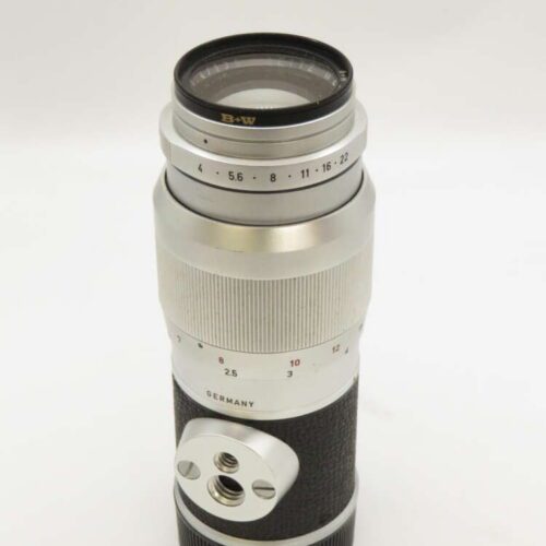 A silver and black vintage camera lens with a textured grip and aperture settings marked from 4 to 22.