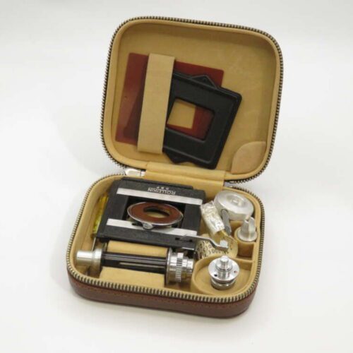 A vintage photography accessory kit with various components, including frames and small metallic parts, inside a brown zippered case.