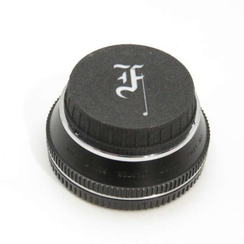 A black camera lens cap with a stylised "F" logo on the top surface.