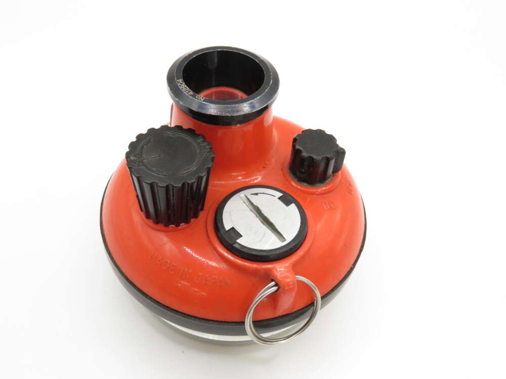 Red mechanical tool with large and small knobs, a circular opening on top, and a metal latch at the bottom.