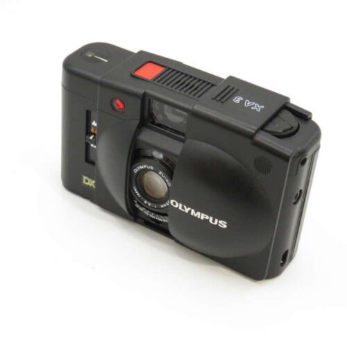 A black Olympus XA 2 film camera featuring a compact design with a visible lens and red shutter button.