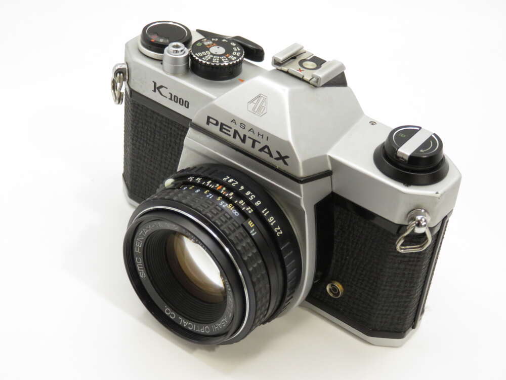 IMG_3874 A vintage Asahi Pentax K1000 film camera with a 50mm lens, featuring a silver and black body with various dials and controls.