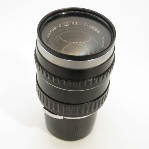A black Nikon Nikkor-Q 135mm f/3.5 camera lens with visible markings and focusing ring on a plain white background.