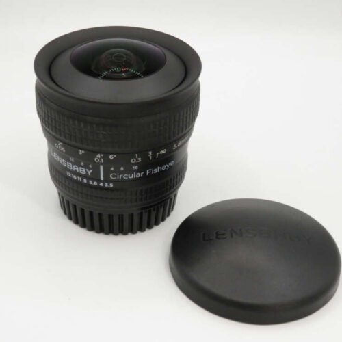 A Lensbaby Circular Fisheye camera lens with its cap placed beside it on a white surface.