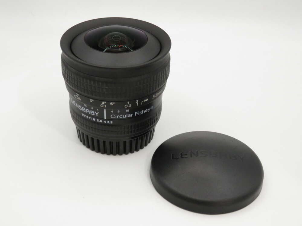 IMG_3921 A Lensbaby Circular Fisheye camera lens with its cap placed beside it on a white surface.