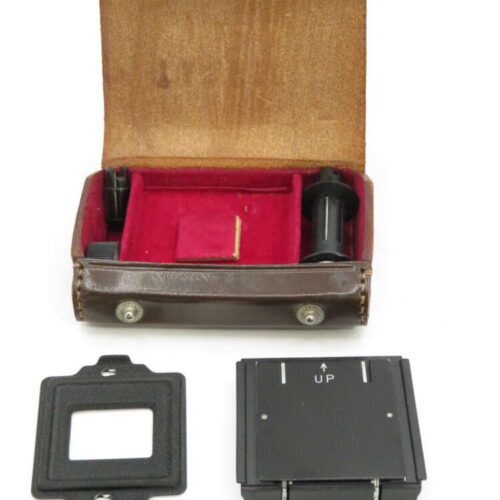 A vintage camera accessory kit with a brown leather case, red interior, black film spool, and a film adapter marked "UP".
