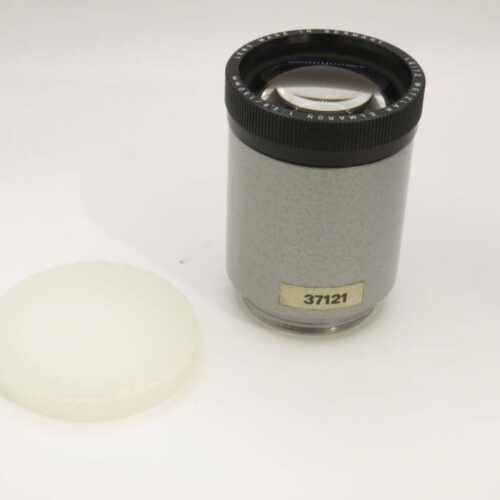 A cylindrical, grey camera lens labeled "37121" sits upright with a white plastic cap beside it.