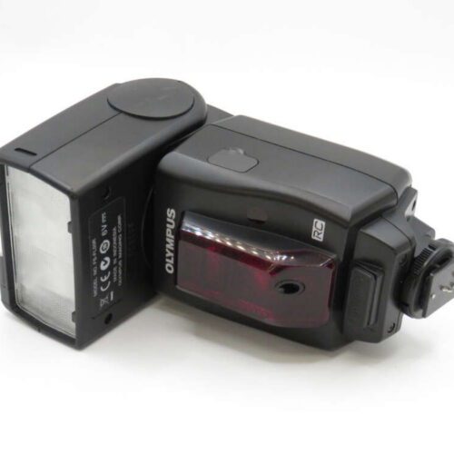 Black Olympus camera flash unit lying on its side on a white surface.