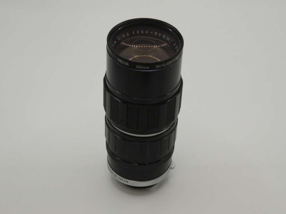 IMG_3973 A vintage telephoto camera lens with a Hoya Skylight filter, displaying markings 1:3.5 f=135mm, 90mm Japan, on a plain backdrop.