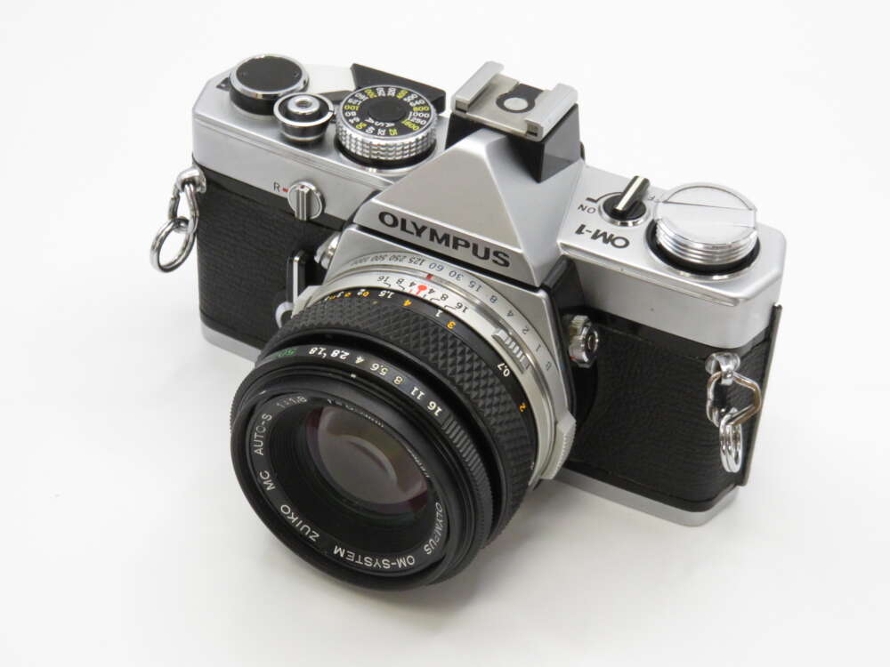 IMG_3979 A vintage Olympus OM-1 camera with a sleek design and leather grip, featuring a lens and visible dials.