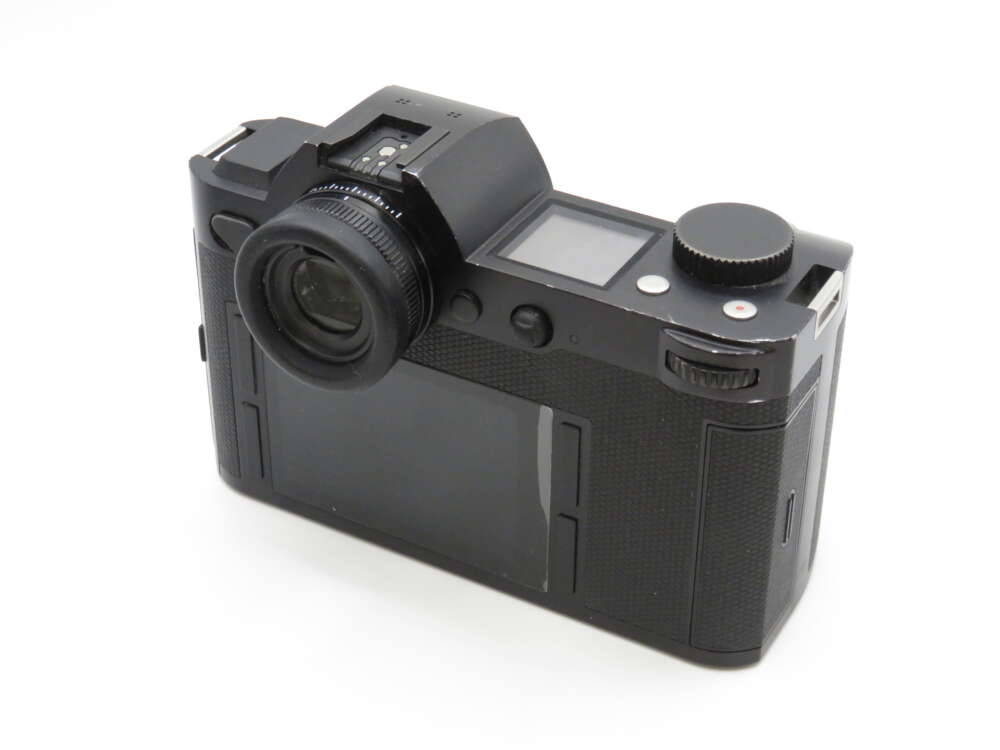 A black digital camera with a protruding viewfinder and a large rear screen, featuring several buttons and dials.