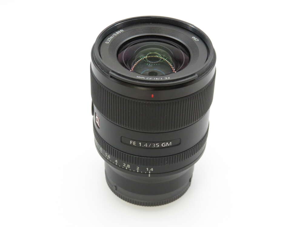 A camera lens with "FE 1.4/35 GM" markings, featuring a textured focus ring and a visible aperture scale.