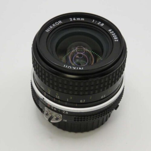 A Nikon Nikkor 24mm f/2.8 camera lens with a black ribbed exterior and clear glass elements reflecting light.