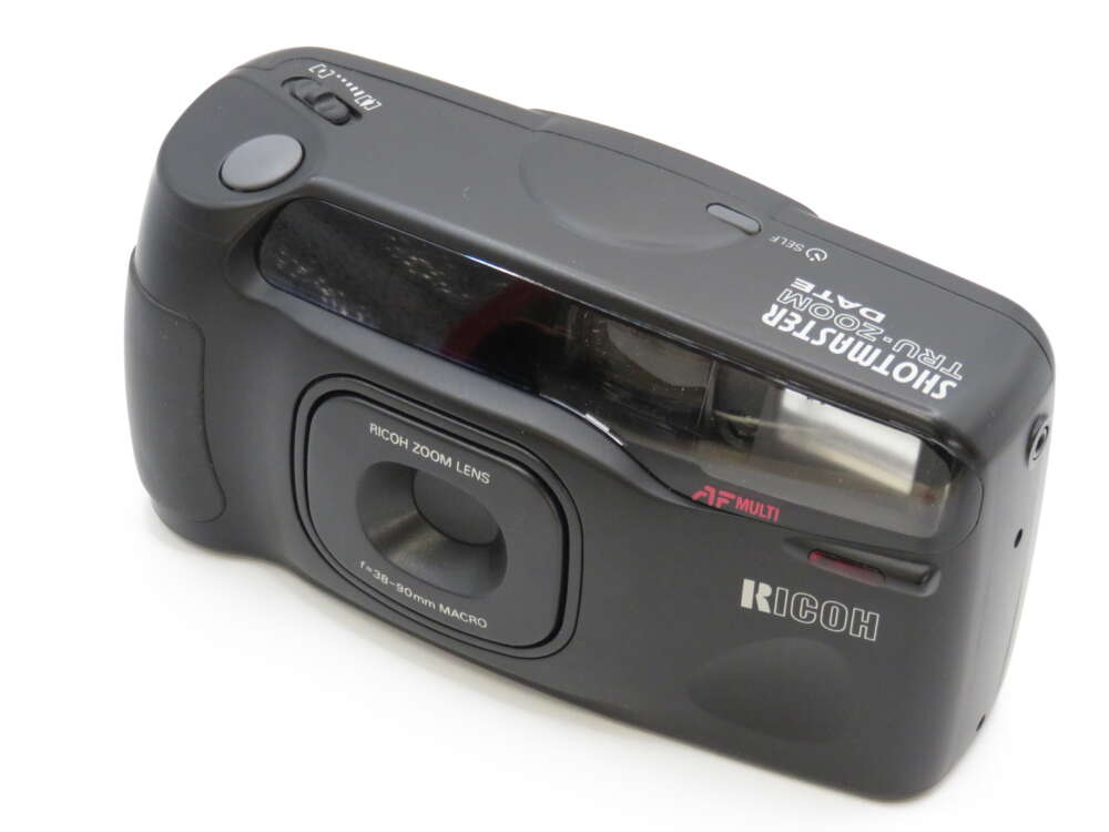IMG_4032 A Ricoh film camera with a textured black body, zoom lens, and flash compartment.