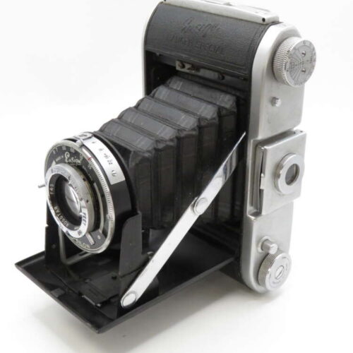 A vintage folding camera with a bellows design and metal casing, featuring a prominent lens and knob controls.