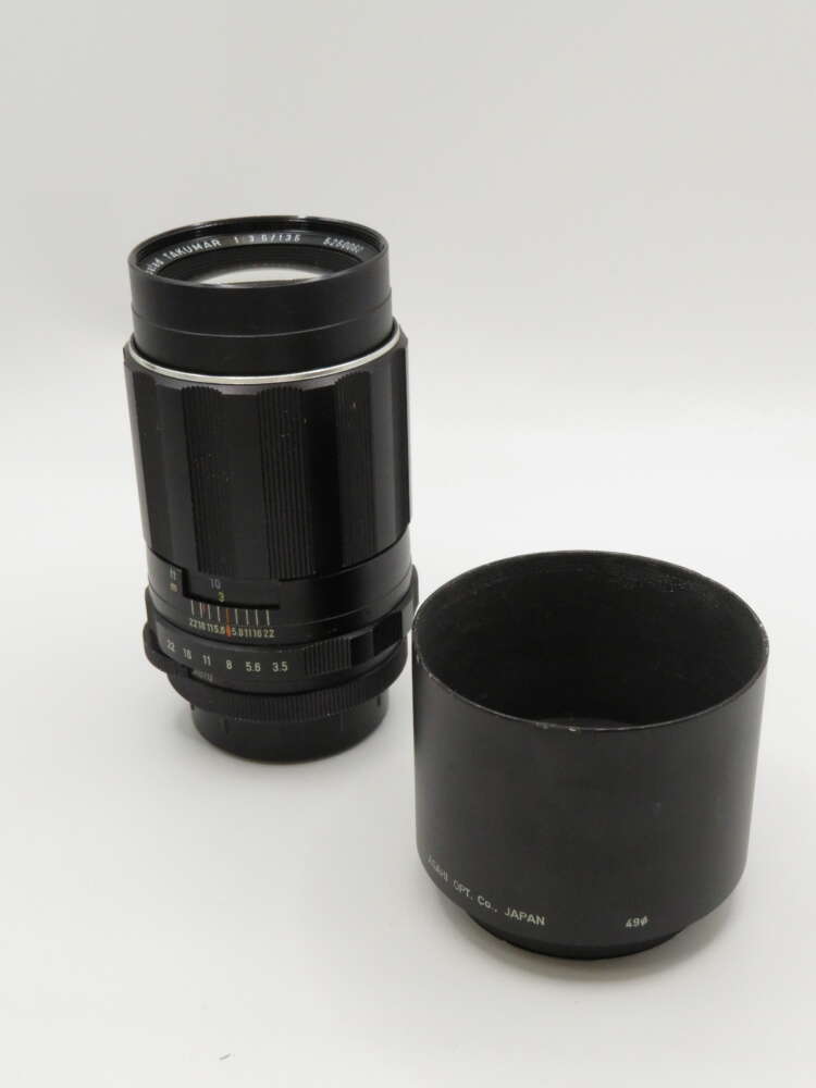 IMG_4076 A black camera lens with a detachable hood placed beside it on a white background.