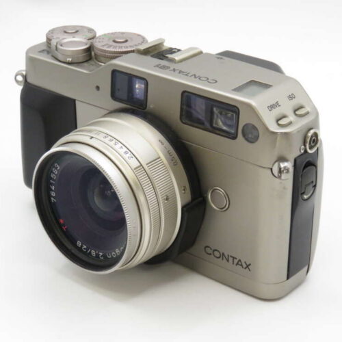 A silver Contax film camera with a large lens and multiple dials on top, set against a plain background.
