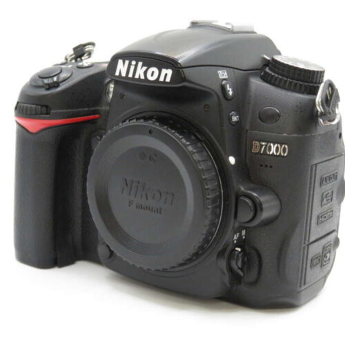 A black Nikon D7000 DSLR camera with various buttons and a lens cap on, angled to the right.