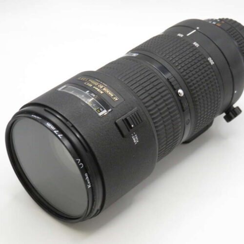 A black telephoto camera lens with marked zoom settings, lying on a white surface.