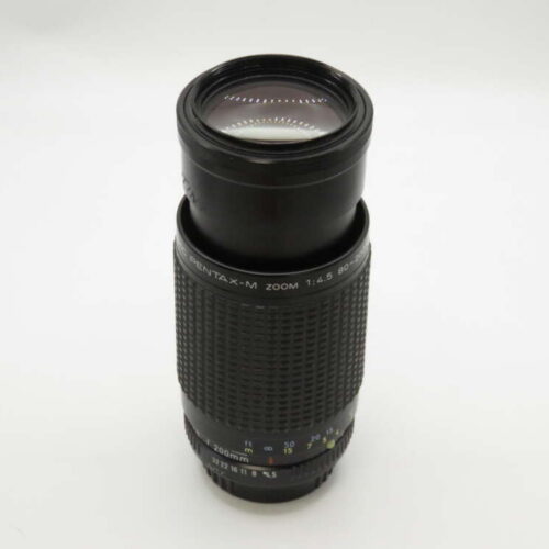 A black Pentax-M zoom lens with markings and numbers on a plain background.