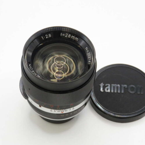 A Tamron 28mm f/2.8 camera lens with its cap beside it on a white surface.