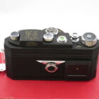 A vintage black camera with various knobs and dials, marked "Widelux F8 Made in Japan," resting on a red surface.