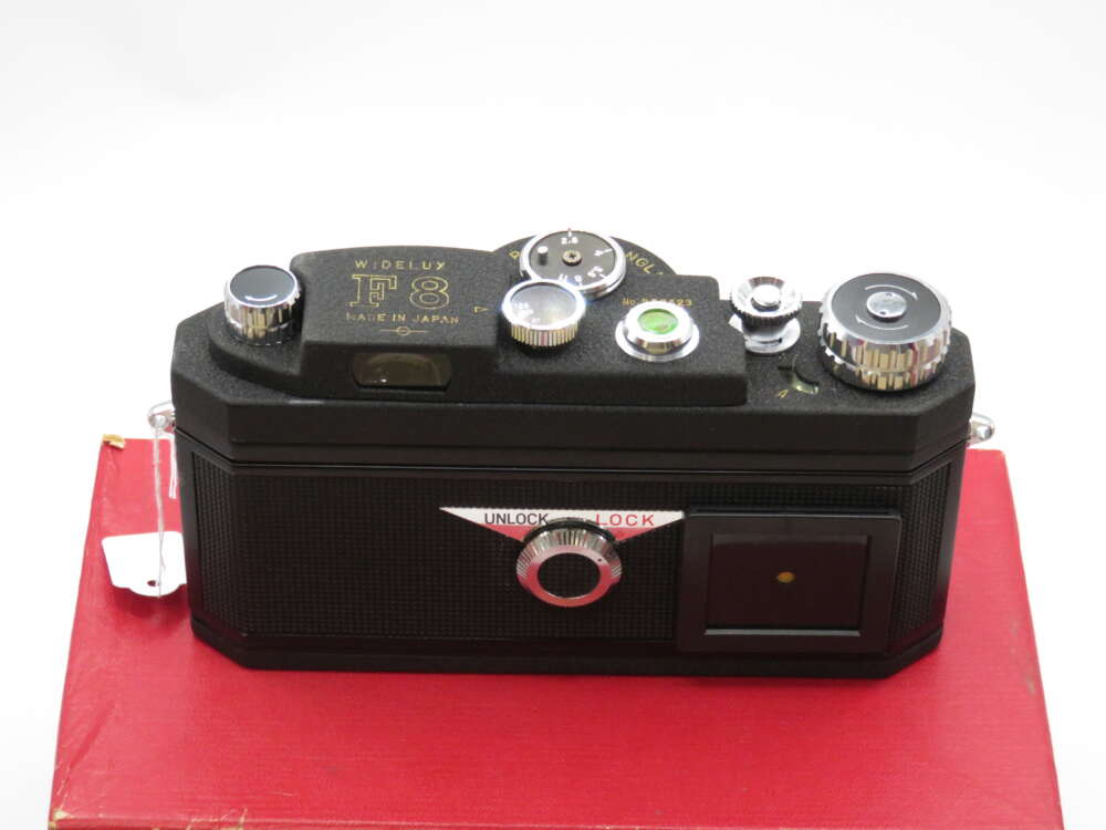 A vintage black camera with various knobs and dials, marked "Widelux F8 Made in Japan," resting on a red surface.