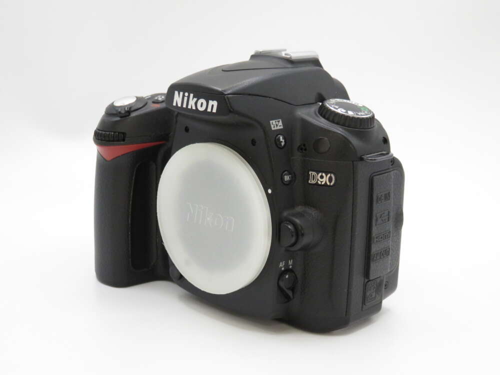 IMG_4170 A Nikon D90 DSLR camera body with a protective cap over the lens mount, set against a plain white background.