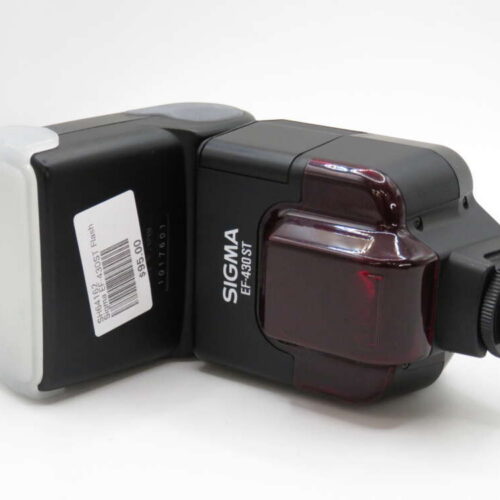 A Sigma EF-430ST external camera flash with a red lens and attached price tag, resting on a white surface.