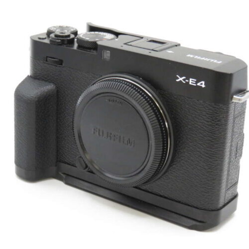A black Fujifilm X-E4 camera with a textured grip and visible dials, viewed from a front angle with the lens cap on.