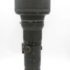 A large Nikon camera lens with a matte black exterior, featuring multiple adjustment rings and a wide lens hood.
