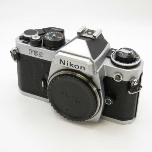 Silver and black Nikon FE2 film camera with a Vivitar lens cap, placed on a plain white background.