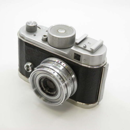 A vintage film camera with a silver and black body, featuring a prominent lens and various manual dials.