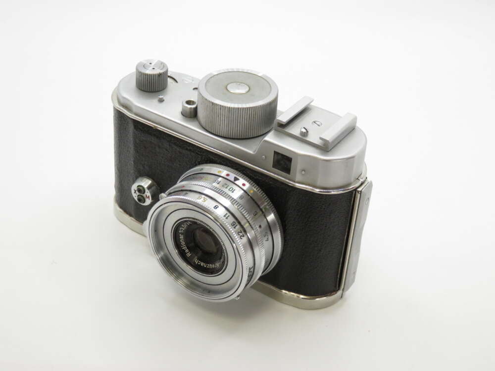 IMG_4223 A vintage film camera with a silver and black body, featuring a prominent lens and various manual dials.