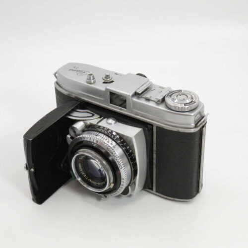 A vintage folding camera with a silver top, black textured body, and attached bellows.