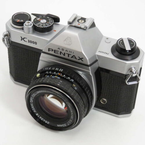 A silver and black Asahi Pentax K1000 camera with a 50mm lens, featuring dials and a viewfinder on top.