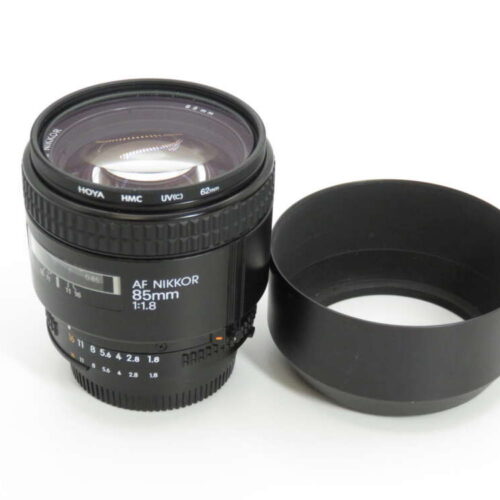 An AF Nikkor 85mm f/1.8 camera lens with its lens hood placed beside it.