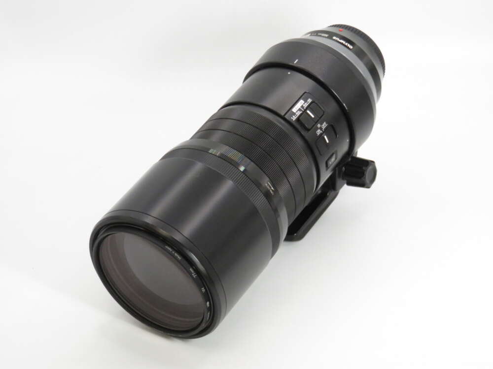 IMG_4321 A large black camera lens with a tripod mount and various control switches on a white background.