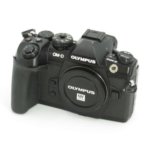 A black Olympus OM-D digital camera with various control dials and buttons, placed on a white surface.