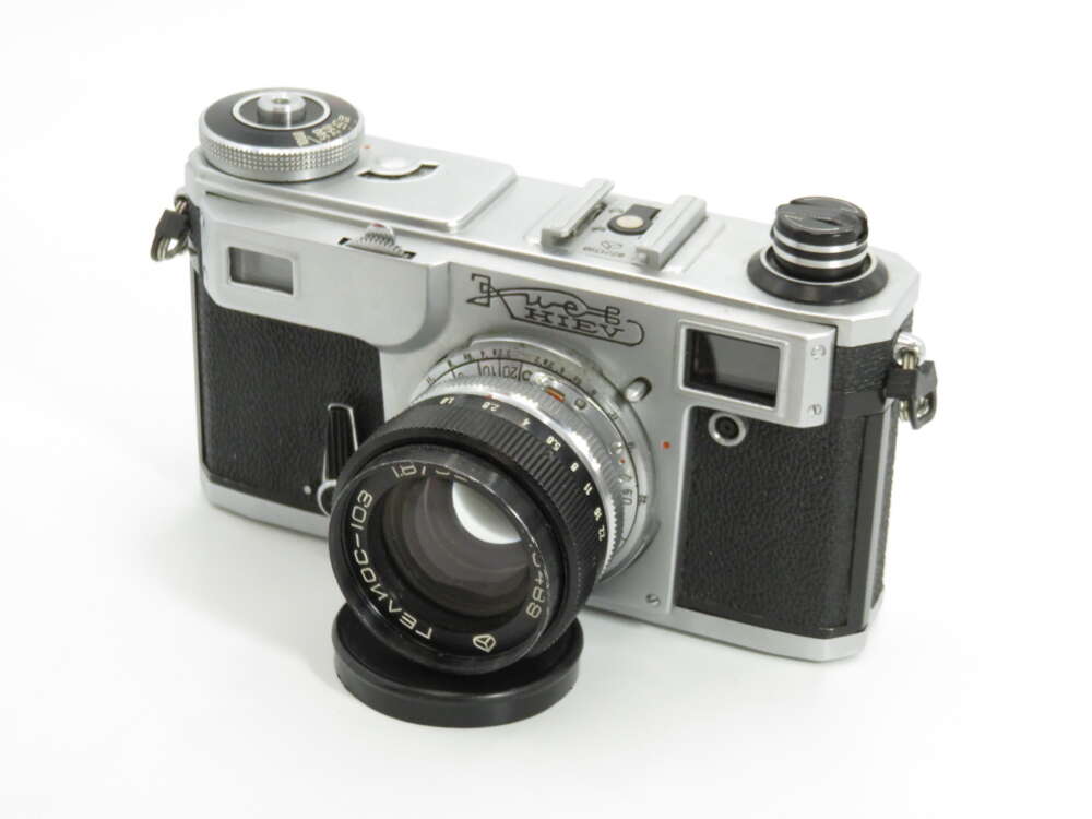 IMG_4334 A vintage rangefinder camera with a silver top, black body, and an attached lens on a white background.